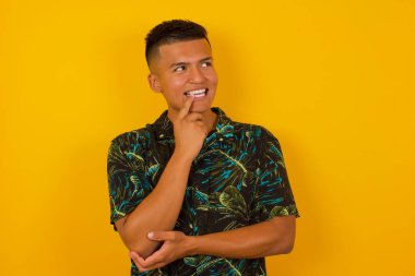 Hayalperest İspanyol bir erkek, düşünceli bir yüz ifadesi var, kameraya bakıyor, elini yüzüne yakın tutuyor, parmağını ısırıyor, hoş bir şey düşünüyor, duvara karşı poz veriyor..