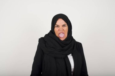 Vücut dili. Siyah tesettürlü stresli Müslüman kadın gri duvara karşı poz veriyor, kaşlarını çatıyor, bir şeyden tiksindiğini gösteriyor..