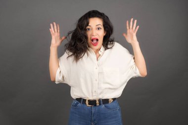 Gayri resmi giyinmiş güzel esmer kadının kafası karışmış. Gri arkaplanda duruyor.  