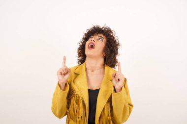 Olumlu ifadeli, kaygısız, çekici bir kadın, her iki işaret parmağıyla da işaret ediyor, günlük kıyafetler giymiş, geniş bir tebessüme sahip, gri arka planda soyutlanmış. Şuraya bakın, lütfen..