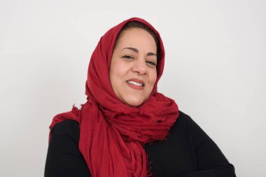 Utangaç, olgun bir kadın kameraya bakıp gülümsüyor. Stüdyoda poz veren başörtüsü takan orta yaşlı bir Arap kadın.