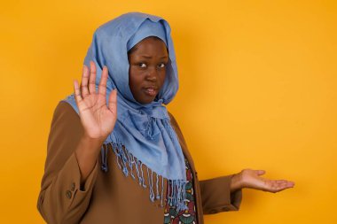 Genç, mutlu, Afro-Amerikan Müslüman kadın parmağını kaldırıyor ve diğer eliyle işaret ediyor. İyi iş çıkardın. Günlük giysiler giyiyor..