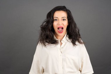 Güzel esmer kadın, gri arka planda gelişigüzel giyinmiş dil gösteriyor..  