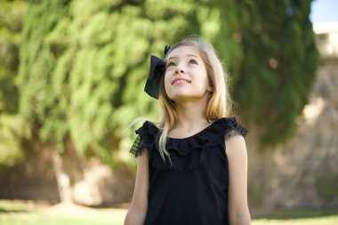 Esrarengiz bir gülümsemeyle yukarı bakan siyah elbiseli çekici kızın portresi. Güzel gülümseyen kız parkta dikiliyor. 