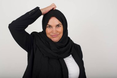 Tüh, ne yaptım ben? Siyah tesettürlü güzel Müslüman kadın korkmuş ve pişmanlık dolu bir ifadeyle el ele tutuşuyor. Gri arka planda dikilen günlük giysiler giyiyor..