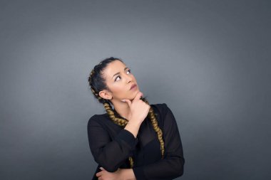 Düşünceli gülümseyen kızın portresi elini çenesinin altında tutuyor, yan bakıyor, ilgi çekici bir şey düşünüyor ya da merak ediyor, sıradan giyiniyor, gri stüdyoya karşı poz veriyor. Karar alma kavramı.