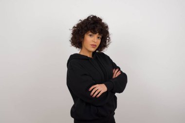 Gri duvara yaslanmış, kolları çaprazlanmış, sıradan kıyafetler giymiş güzel bir bayan. Kameraya bakıp gülümsüyor. Kendine güvenen başarılı bir kadın..