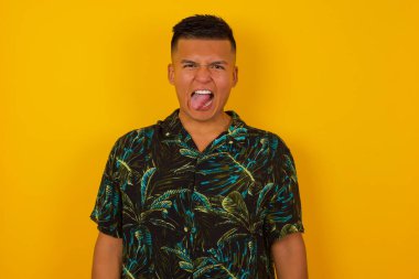 Gülümseyen ve dil gösteren mutlu ve komik yüzlü yakışıklı İspanyol adam. Günlük giysiler giyip stüdyonun arka planında dikiliyor..