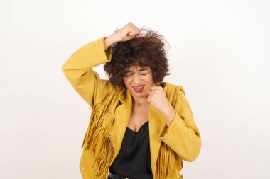 Çekici genç bir kadın zaferi kutluyor yumruklarıyla havaya yumruk atıyor ve arka plandaki gri bir stüdyonun üzerinde ışıldayan dişli bir gülümsemeyle fotokopi çekiyordu.