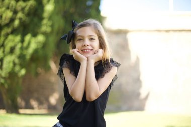 Hayalperest genç Avrupalı kız ellerini çenesinin altında tutuyor, mutlu bir ifadeyle bakıyor, dişlek bir gülümsemesi var.