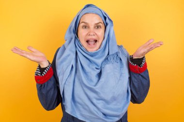 Başarı, başarı konsepti. Neşeli orta yaşlı, tesettürlü Müslüman kadın ellerini kaldırıyor, mutluluk dolu gözleriyle büyük başarılarını kutluyor.. 