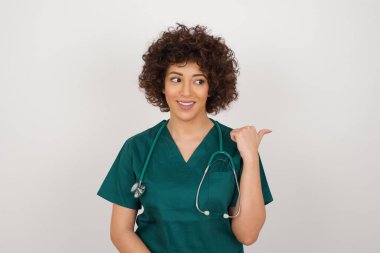 Şaşırmış ifadesi olan doktor kadın baş parmağıyla gri arka planda bir şey gösteriyor. Reklam kavramı.