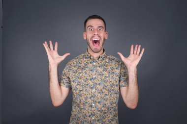 Yakışıklı bir adamın portresi kameraya heyecanla bakar, ellerini başının üstünde tutar, beklenmedik bir şey fark eder, gri duvarın üzerinde izole bir şekilde..