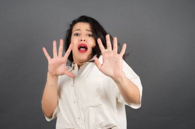 Gayri resmi giyinmiş güzel esmer kadın korkuyor. Gri arkaplanda duruyor. 