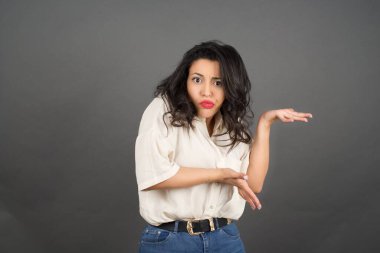 Güzel esmer kadın bir şey gösteriyor. Gri arkaplanda duruyor. 