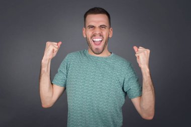 Sıradan tişörtler giyen, kollarını kaldıran, yumruklarını sıkan, sevinç ve heyecanla haykıran güçlü ve kararlı genç bir erkeğin portresi. Zafer, başarı ve başarı kavramı.