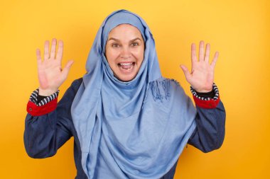 Neşeli, şanslı, orta yaşlı, tesettürlü Müslüman kadın. Tezahürat yapıyor, başarıyı kutluyor, sıkıca sarılmış ellerle evet diye bağırıyor.