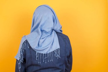 Orta yaşlı, tesettürlü Müslüman bir kadının duvarın önünde duruşu. Stüdyo Çekimi. 