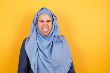 Vücut dili. Orta yaşlı, tesettürlü, duvara karşı poz veren, kaşlarını çatan, bir şeyden tiksinen orta yaşlı Müslüman kadın..