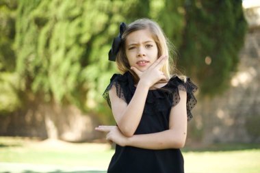 Endişe. Siyah elbiseli güzel bir kızın kavramsal görüntüsü. Ağzını elleriyle kapatıyor ve parkta dikiliyor. 