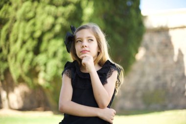 Düşünceli, düşünceli genç bir kız elini çenesinin altında tutuyor. Düşünceli bir şekilde yukarı bakıyor, günlük kıyafetler giyiyor.