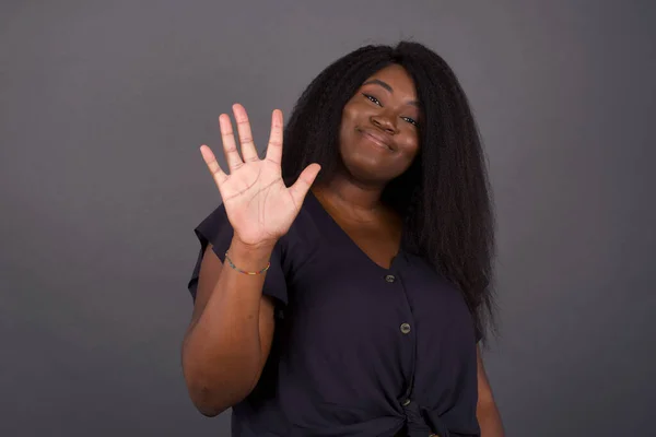 年轻的非洲裔美国妇女靠着灰墙站着 用五号手指指指指点点 自信而快乐地微笑着 — 图库照片