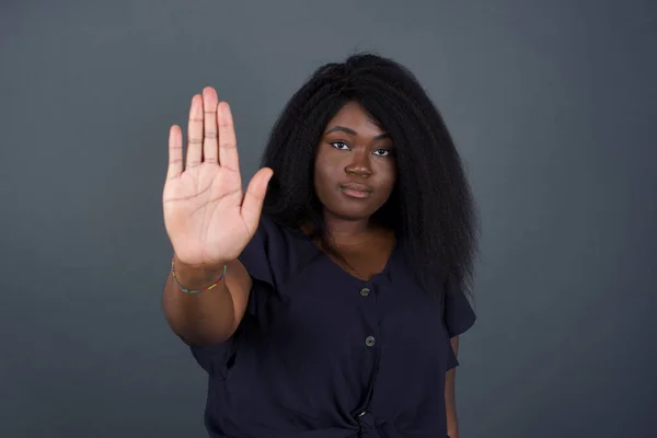 African American woman doing stop gesture with palm of the hand. Warning expression with negative and serious gesture on the face isolated over gray background.