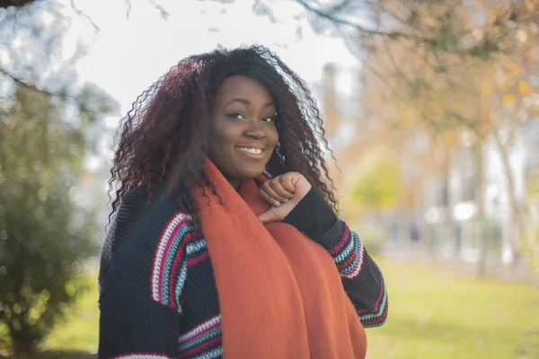 秋の公園で自分自身を指すカラフルなセーターを身に着けている長い髪の美しいアフリカ系アメリカ人女性 — ストック写真