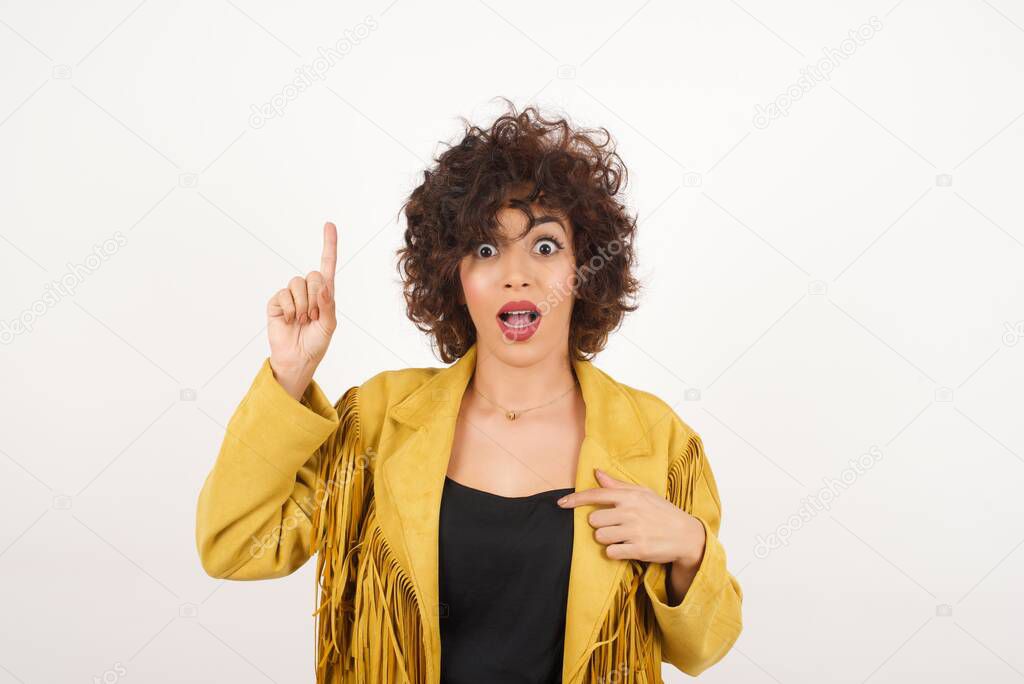 Positive glad  woman   says: wow how exciting it is, has amazed expression, indicates something. Joyful pretty young woman demonstrates something. One hand on her chest and pointing with other hand.