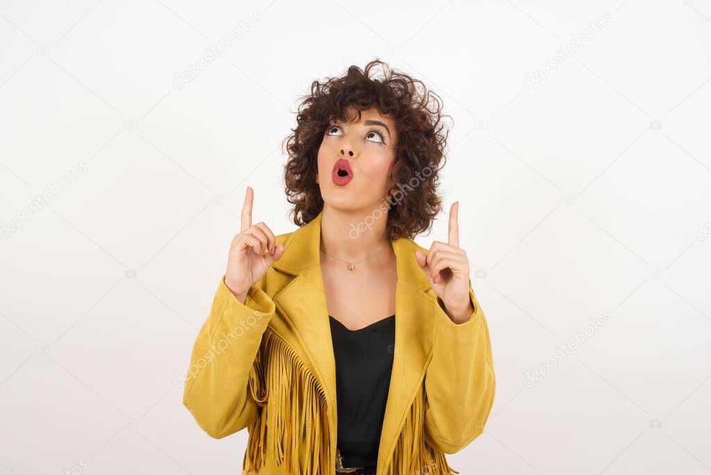 Portrait of beautiful elegant woman over isolated background being amazed and surprised looking and pointing up with fingers showing something strange.