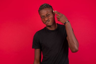 Mutsuz sarışın genç erkek silah atışı taklidi yapıyor intihar jesti yapıyor iki parmağını şakaklarda tutuyor günlük kıyafetler giymiş şaşkın yüz ifadesi içeride duruyor..