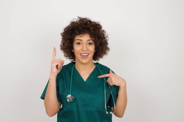 Tıbbi üniforma giyen güzel Arap doktor kadın bir şey ima ediyor. Bir eli göğsünde ve diğer eliyle işaret ediyor..