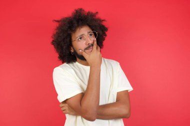 Kızıl duvara karşı düşünen afro saçlı genç bir adam.   