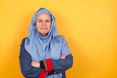 Şık, orta yaşlı, tesettürlü Müslüman bir kadının izole edilmiş portresi. Ağzını ısırıyor ve endişeli ve korkmuş görünüyor. Kol kola, endişe ve şüphe içinde..