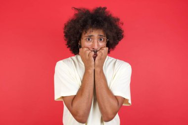 Afro saçlı genç adam kırmızı duvardan korkuyor. 