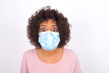 Yüz maskesi takan ve günlük kıyafet giyen kadın beyaz stüdyo arka planında izole edilmiş.