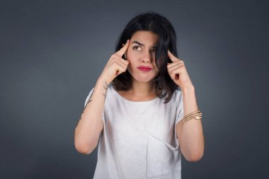 Hayalci beyaz kadın, düşünceli bir yüz ifadesiyle, yüzünü çevirmiş, güzel şeyler düşünüyor, gri duvara karşı poz veriyor..