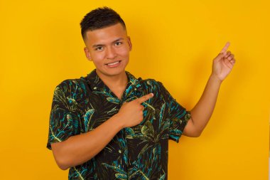 Olumlu ifadeli güzel bir İspanyol genç adam, sıradan giyinmiş, promosyon metnin ya da ilanın için boş fotokopi alanında ön parmağıyla işaret ediyor. Sevimli adam evde tek başına poz veriyor.