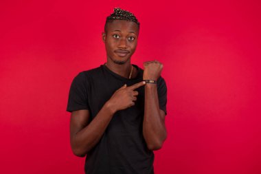 Kırmızı arka planda siyah t-shirt giyen Afro-Amerikan bir adam. Aceleyle zamanı, sabırsızlığı ve gecikmeyi işaret ediyor.