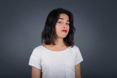 Züppe ifadeli güzel bir kadın dudaklarını kıvırıyor ve kaşlarını kaldırıyor şüpheli ve şüpheci bir ifadeyle şüpheli ve şüpheci bir ifadeyle bakıyor. Gri arka planda kapalı duruyor..