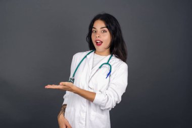 Pozitif memnun doktor diyor ki: Vay be, ne kadar heyecan verici, hayret verici bir ifade, boş alanda bir şey gösteriyor, açık elle izole edilmiş gri arkaplan üzerinde. Reklam kavramı.