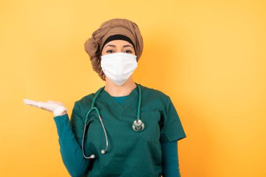 Yüzü maskeli olumlu mutlu Arap kadın doktor der ki: Vay be, ne kadar heyecan verici, hayret verici bir ifade, boş uzayda izole edilmiş arka plan üzerinde açık bir şey gösteriyor.