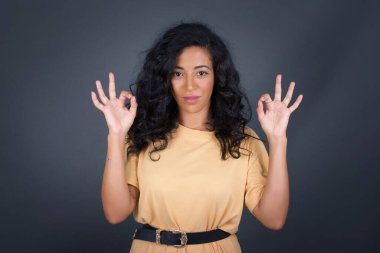 Çekici bir kadının iki eliyle işaret dili göstermesine sevindim. Onayladığına, neşeli bir ifadesi olduğuna sevindim. Gri duvara yaslanarak.