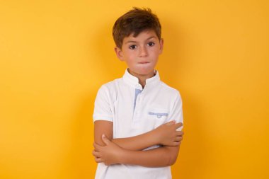 Sarı duvara yaslanmış kolları olan sevimli bir çocuk.  