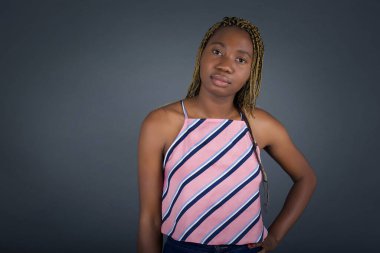 Stüdyoda çekilen neşeli Afro-Amerikalı kadın gri arka planda dururken el ele tutuşup duruyor..