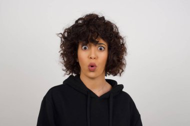 Şaşkınlık ve şaşkınlık ifadesiyle şaşırmış, şaşırmış ve şaşırmış bir şekilde kameraya bakan, sıradan giysiler giyen genç bir kız öğrencinin vesikalığı.