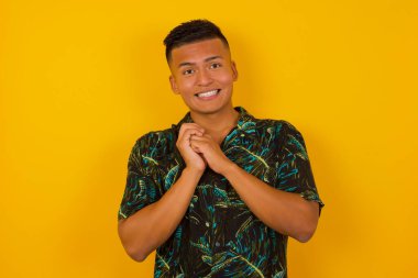 Tatlı yüzlü, rüya gibi, genç, İspanyol bir adam. Ellerini yüzünün yanında çapraz tutuyor. Hoş bir şey için heyecanlı, arka planda poz veriyor..