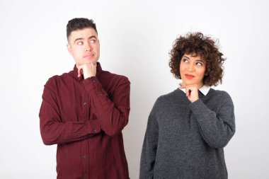  Sıradan kıyafetler giyen çift yan bakıyor, ellerini çenelerinin altında tutuyor, hoş bir şeyler düşünüyor, arka planda poz veriyor..