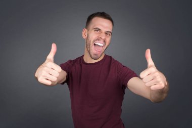 İzole edilmiş bir geçmişi olan genç sarışın adam elleriyle olumlu bir jest yapmayı onaylıyor. Gülümsüyor ve başarı için seviniyor. Kameraya bak, kazanan jest..