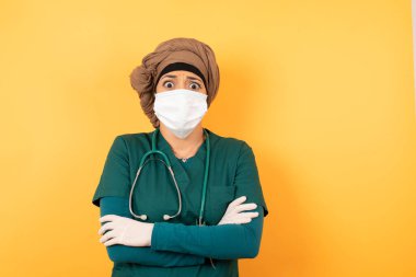 Yeşil üniformalı güzel Müslüman bir kadının izole edilmiş portresi ağzını ısırdı ve endişeli ve korkmuş bir şekilde kollarını kavuşturdu. Endişe ve şüphe..